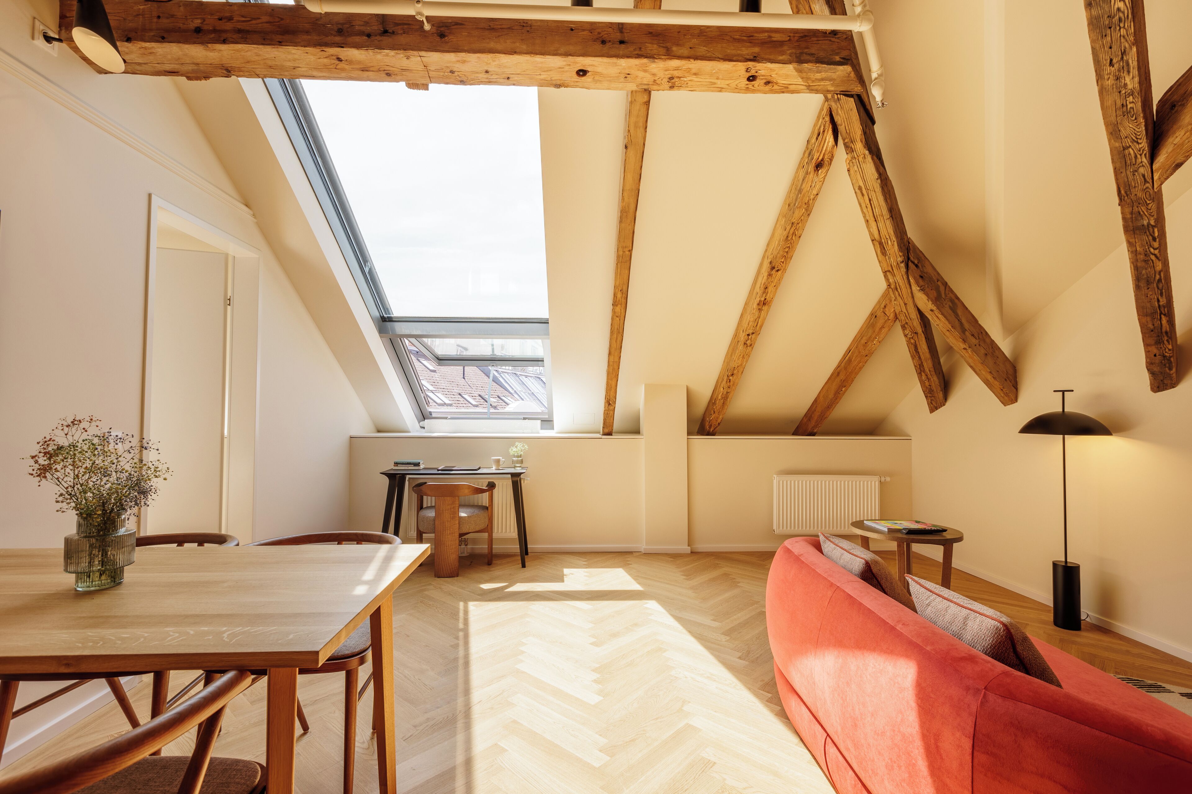 A cozy room with a wooden dining table, a red sofa, and a skylight.