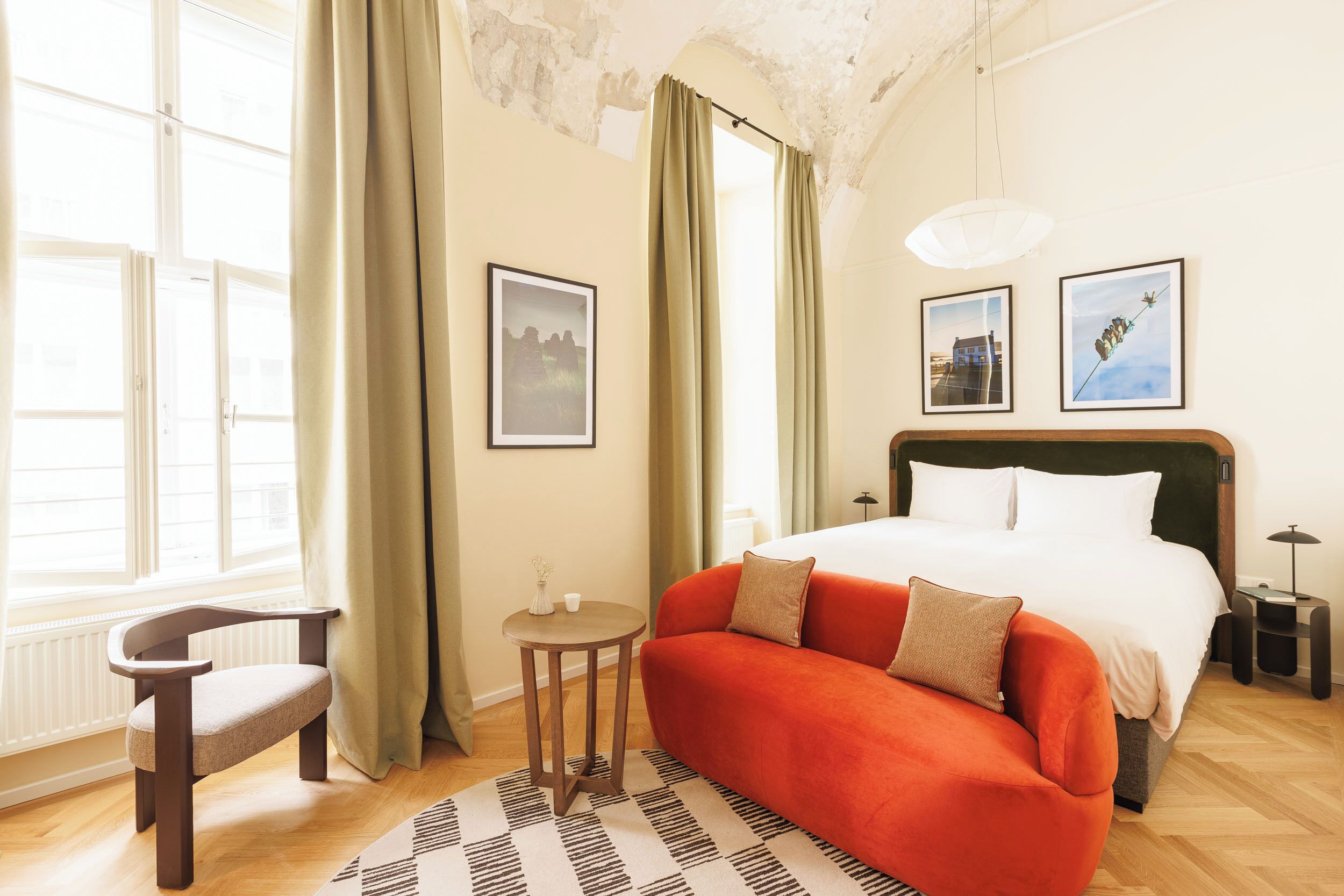 A hotel room with a bed, a sofa, a chair, a small table, and two framed pictures on the wall.