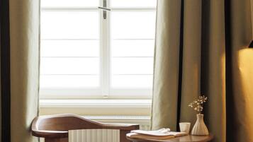 A room with a wooden chair, a small table with a vase, and a window with curtains.