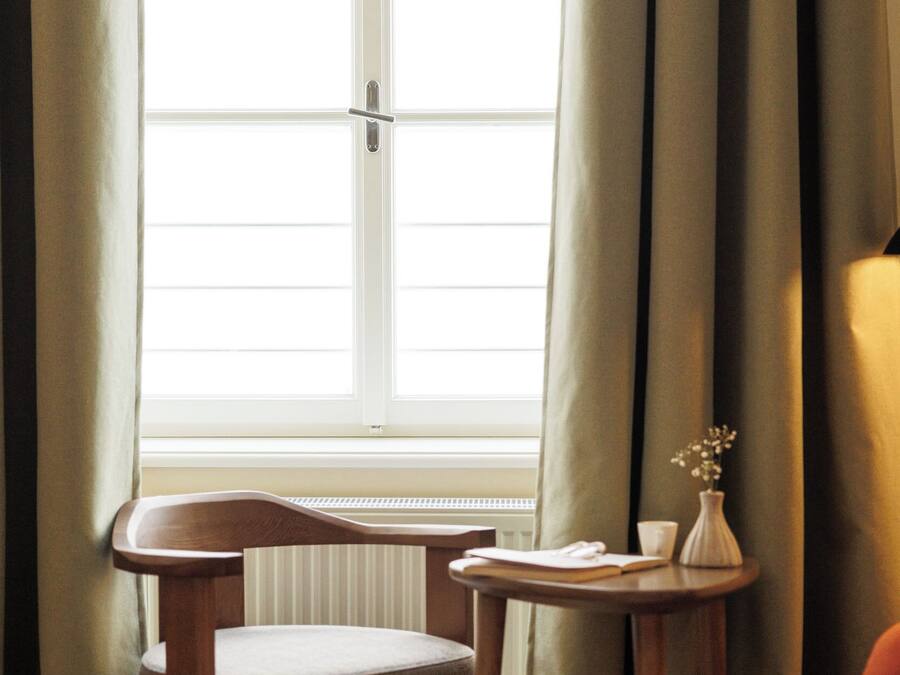 A room with a wooden chair, a small table with a vase, and a window with curtains.