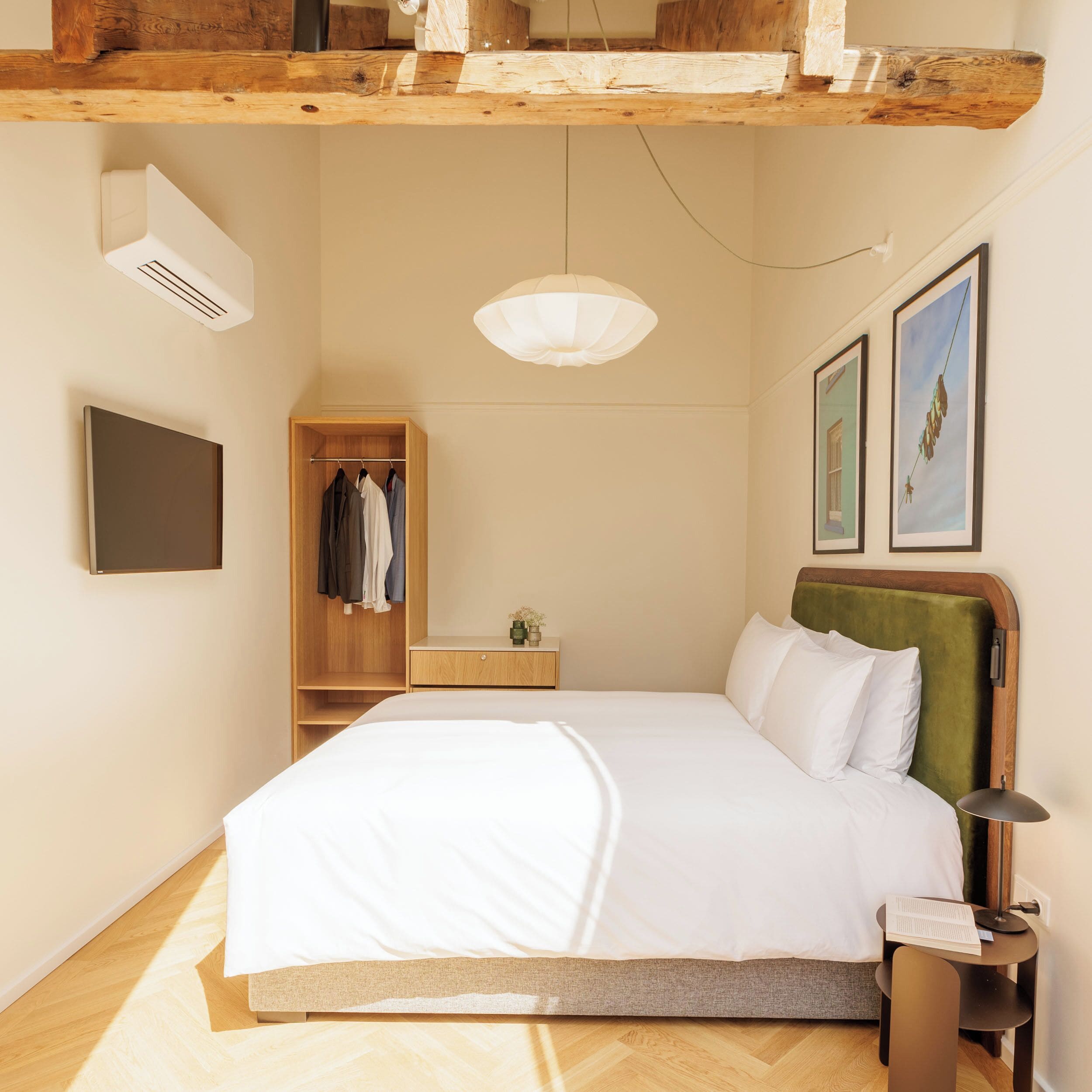 A bedroom with a bed, a wardrobe, a bedside table, a lamp, and a wall-mounted TV.