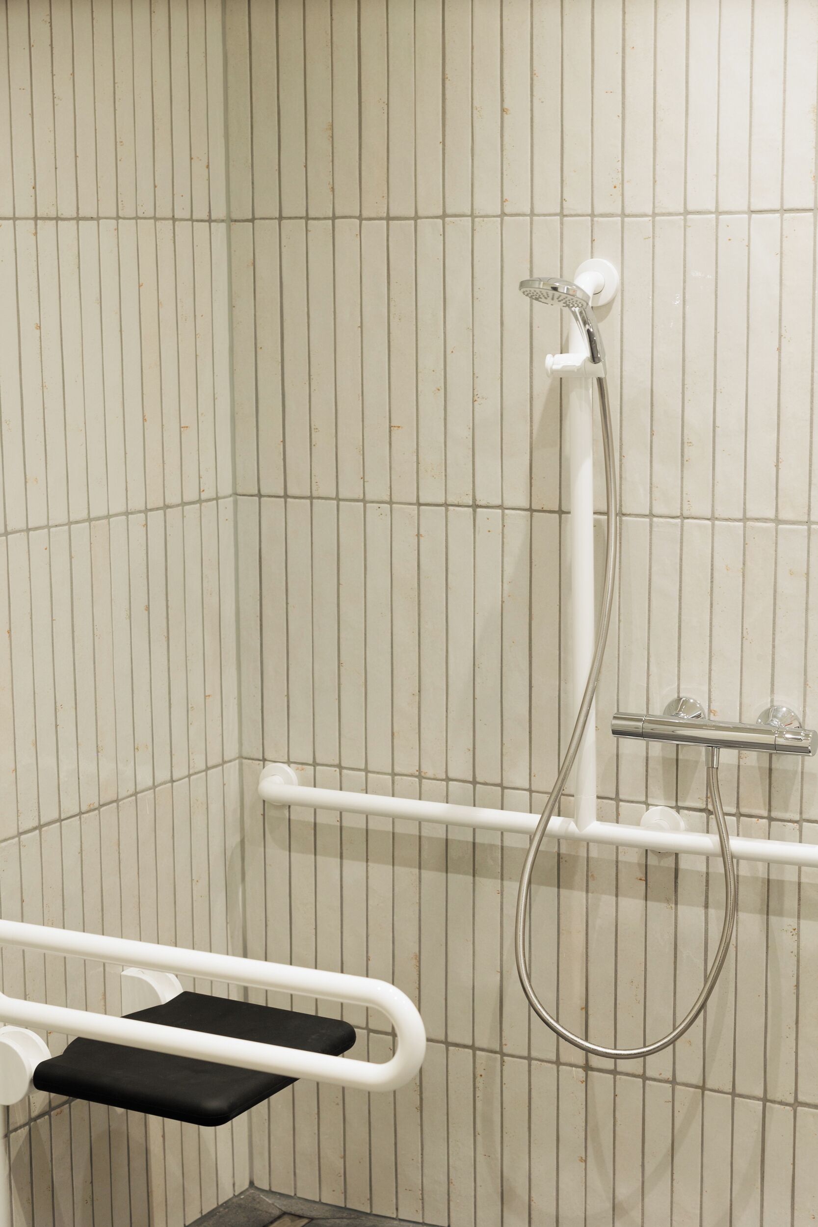 A shower area with a grab bar, a handheld showerhead, and a wall-mounted faucet.