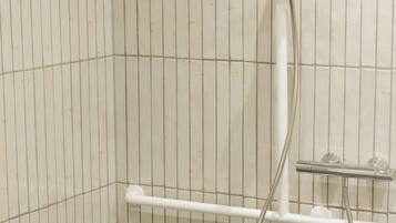 A shower area with a grab bar, a handheld showerhead, and a wall-mounted faucet.