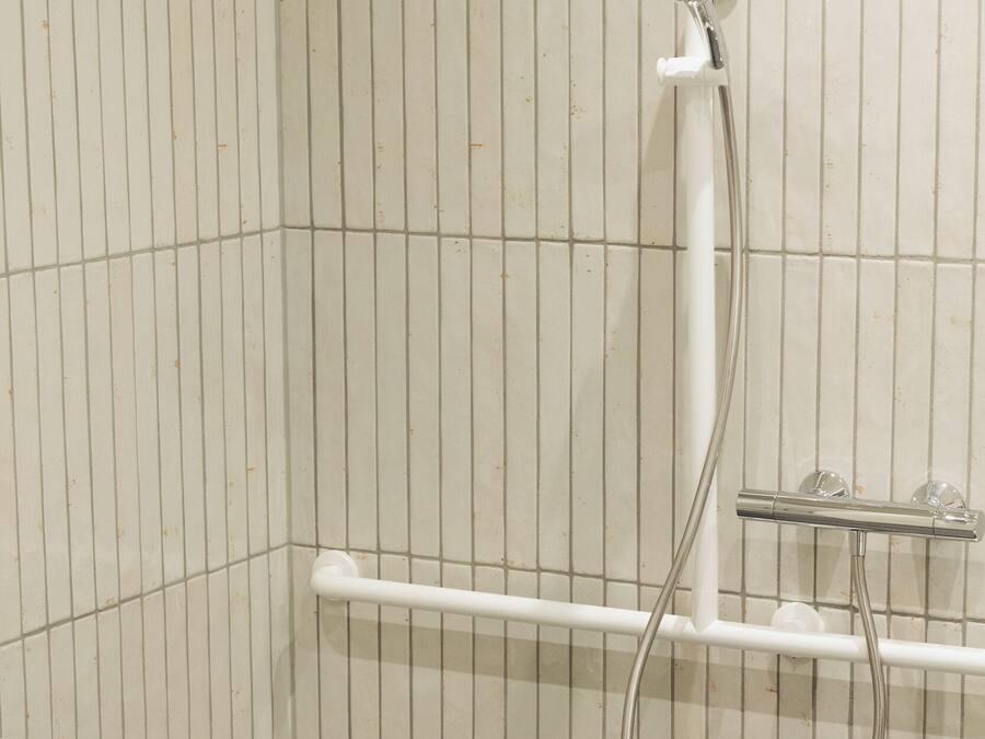 A shower area with a grab bar, a handheld showerhead, and a wall-mounted faucet.