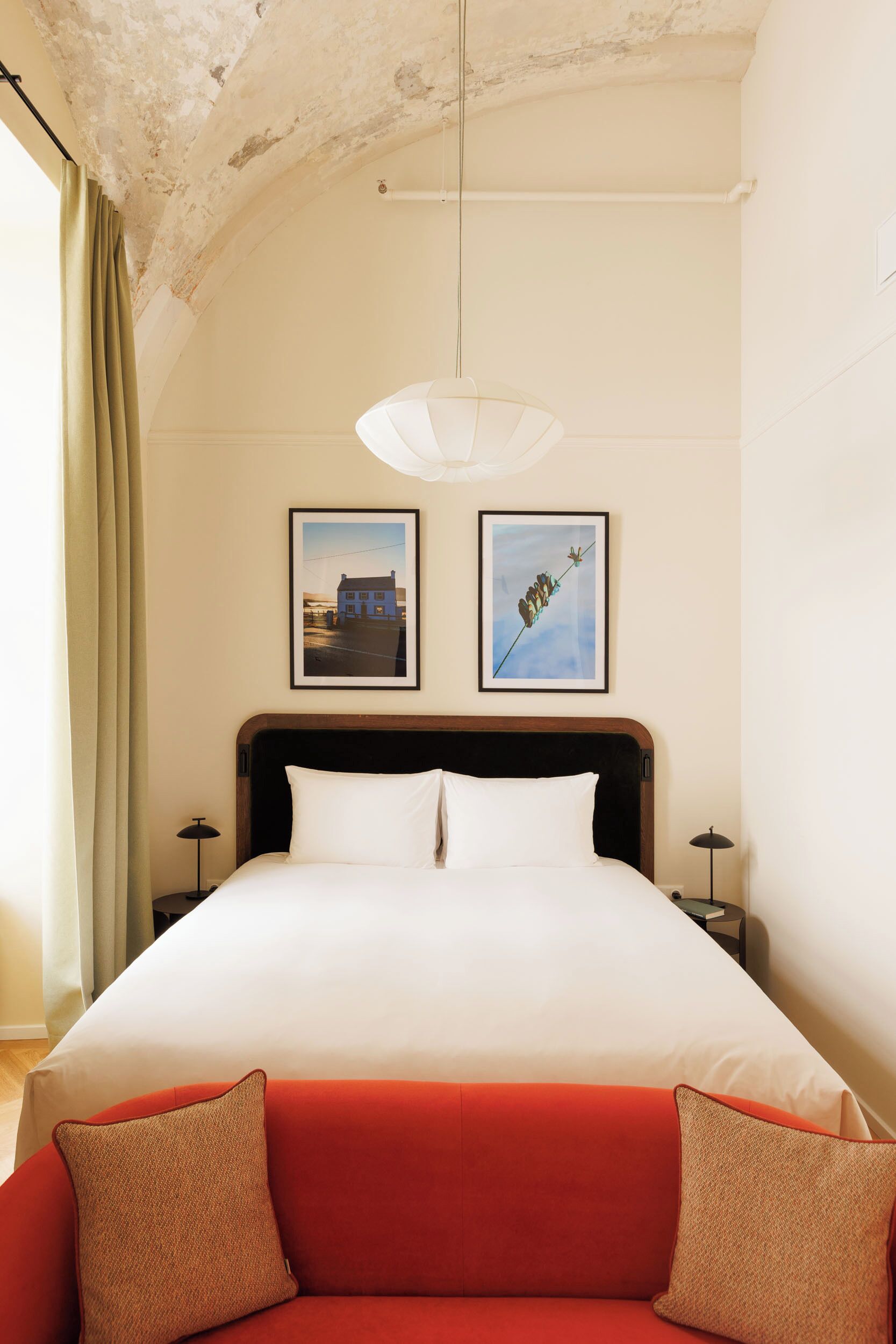Een slaapkamer met een groot bed, twee ingelijste foto’s aan de muur, een rode bank en een plafond met zichtbare balken.