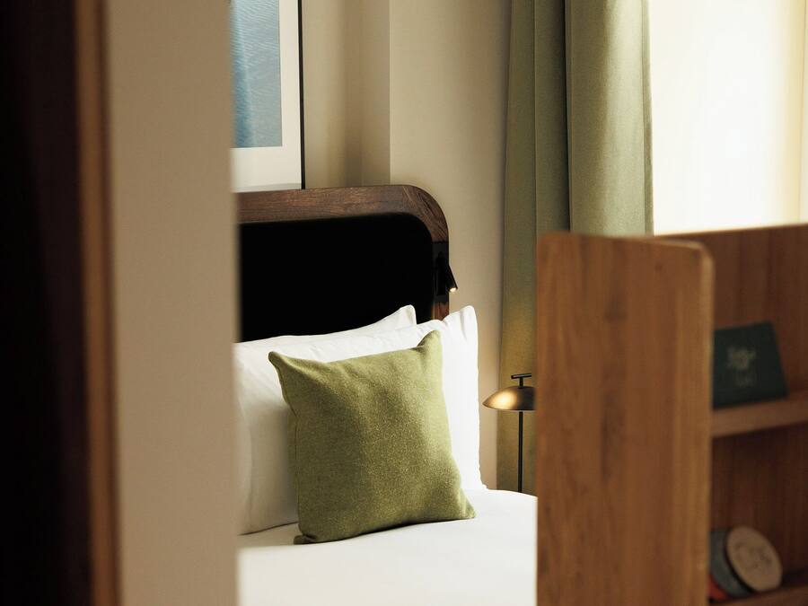 A hotel room with a bed, a nightstand, a lamp, and a wooden chair.