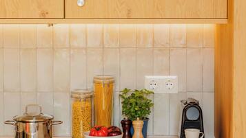 A kitchen with wooden cabinets, a tiled backsplash, a stove, a coffee maker, and a bowl of tomatoes.