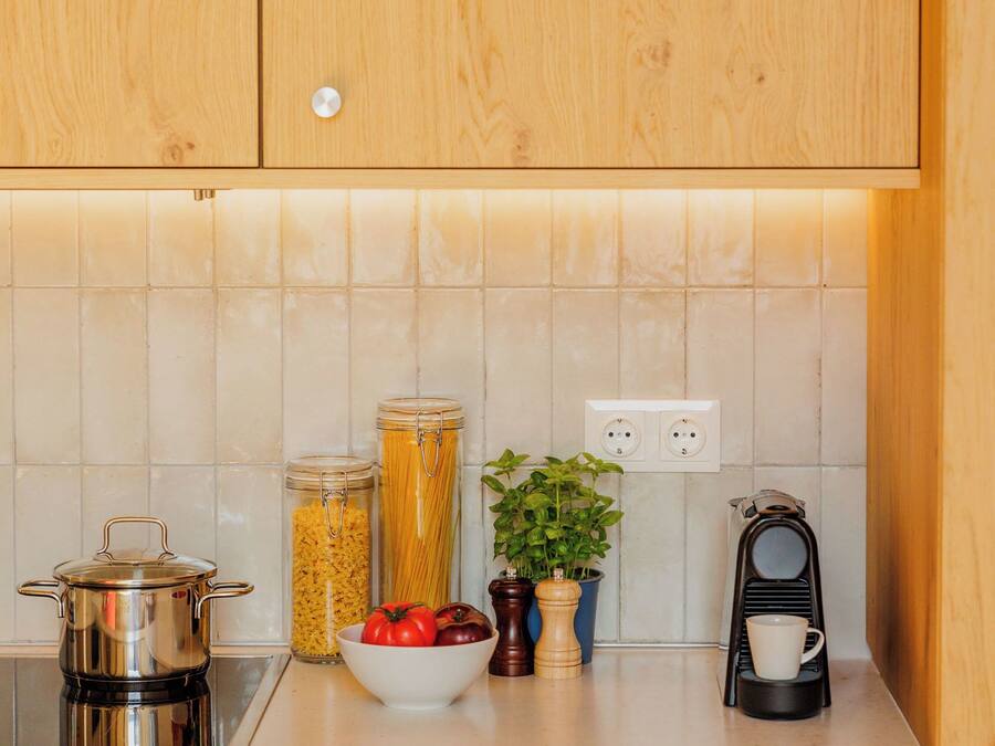 A kitchen with wooden cabinets, a tiled backsplash, a stove, a coffee maker, and a bowl of tomatoes.