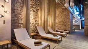 Wellnessbereich mit Holzliegen, einer Ziegelwand und einer modernen Decke mit freiliegenden Rohren.