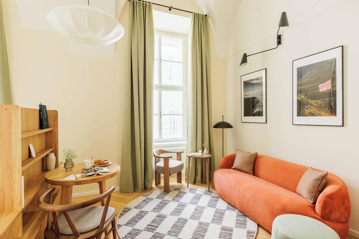 A cozy living room with a sofa, a wooden table, a chair, a lamp, and framed pictures on the wall.