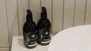 Dos botellas de jabón líquido para manos Wilde sobre una superficie blanca, junto a un lavamanos.