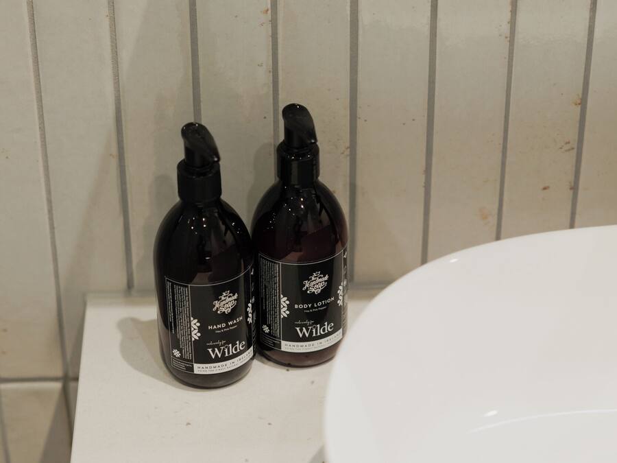 Dos botellas de jabón líquido para manos Wilde sobre una superficie blanca, junto a un lavamanos.