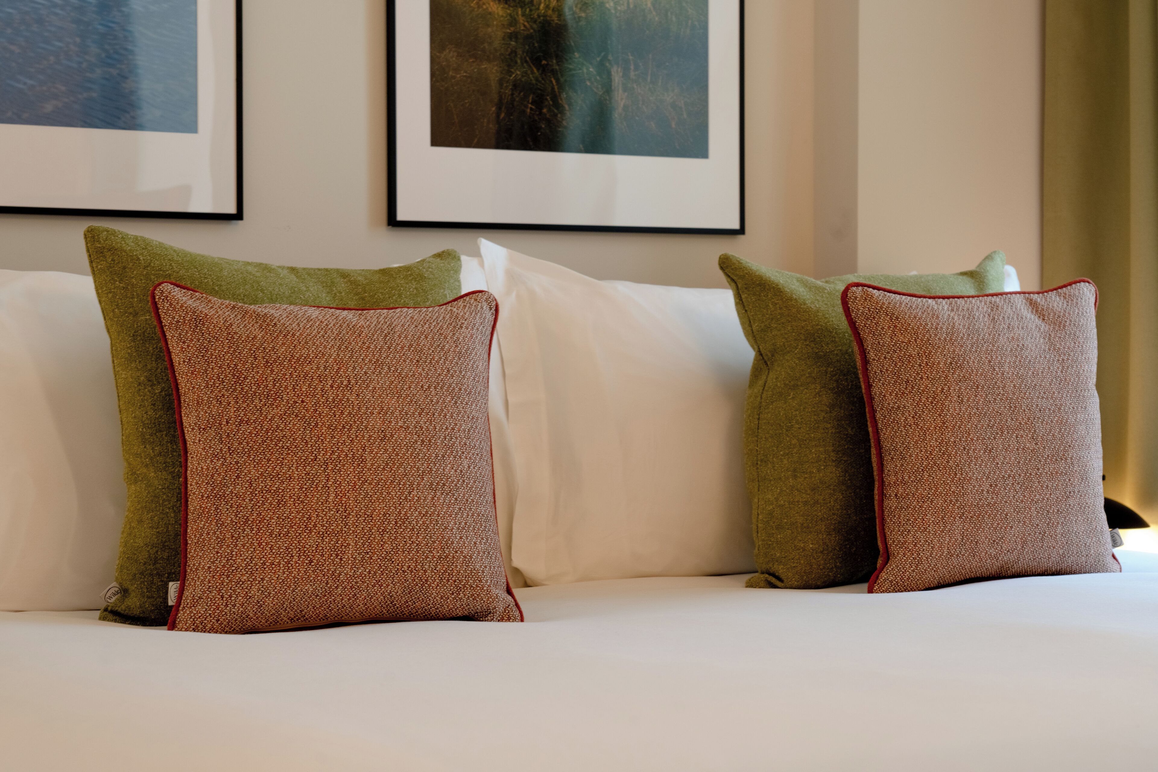 A bed with white linens and two green pillows with red trim.