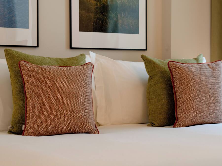 A bed with white linens and two green pillows with red trim.