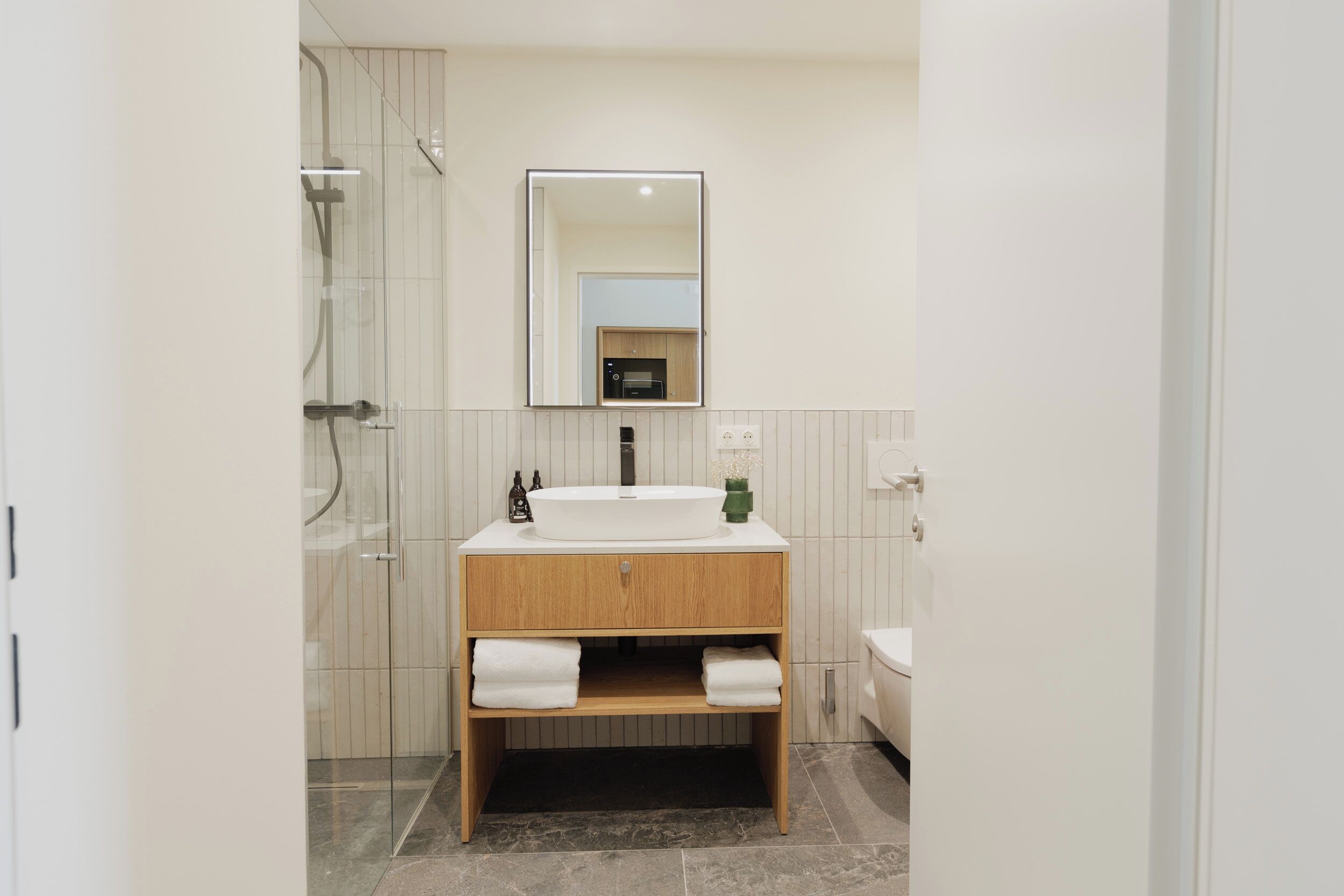 A modern bathroom with a glass shower enclosure, a wooden vanity with a sink, and a mirror.