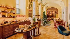 Ein gemütliches Café mit Holztischen, einer zentralen Theke und einem Bücherregal voller Bücher.