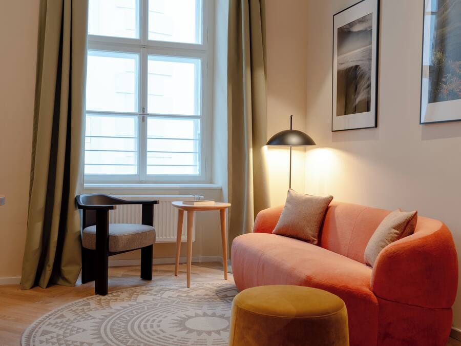 A living room with a sofa, a chair, a small table, a lamp, and a window with curtains.