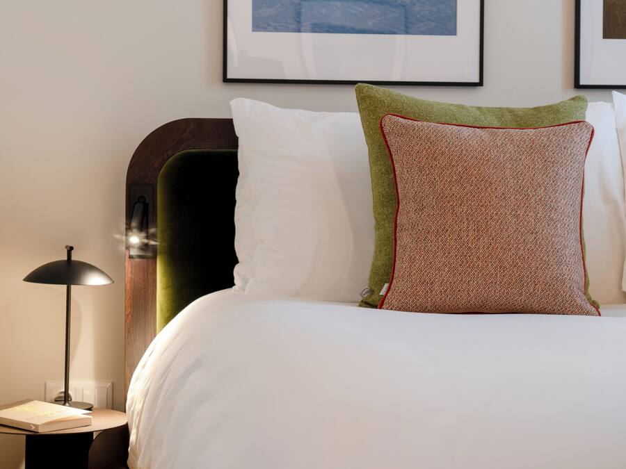 A neatly made bed with white and green pillows, a black floor lamp, and framed artwork on the wall.