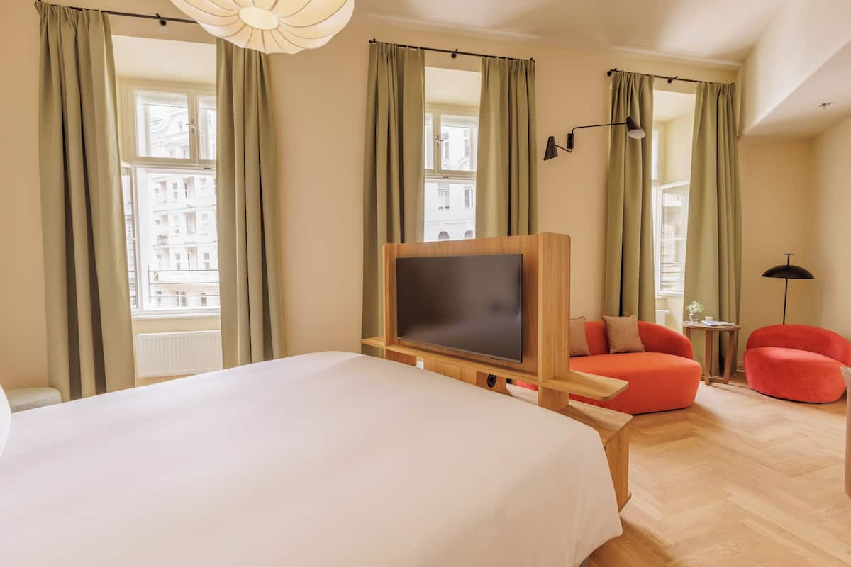 A hotel room with a large bed, a flat-screen TV, a red armchair, and a small table.