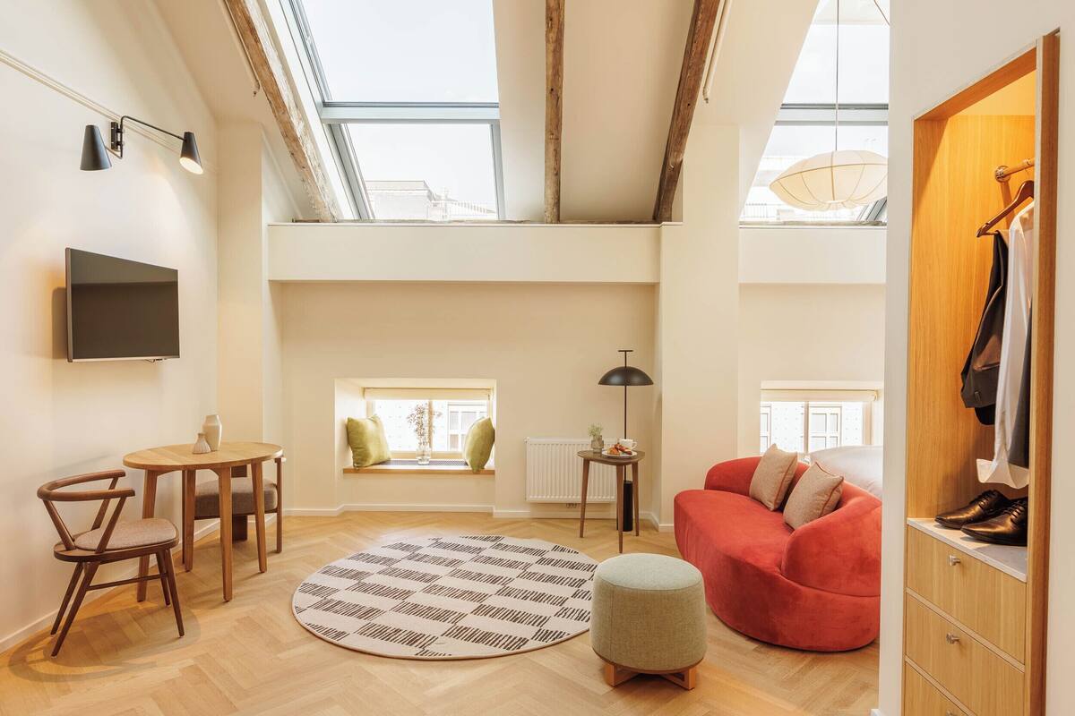 A spacious loft apartment with high ceilings, skylights, a red sofa, a round rug, and a wooden wardrobe.