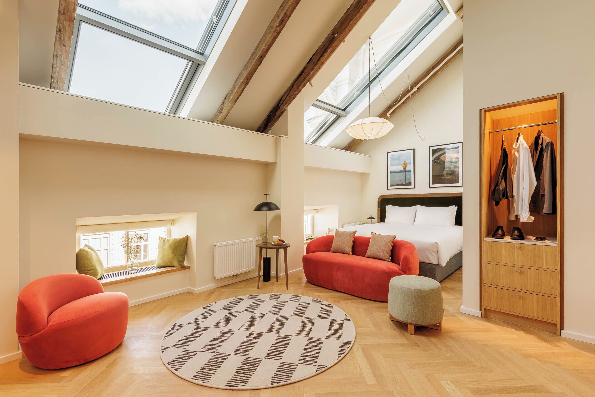 A spacious loft bedroom with skylights, a red sofa, a round rug, and a wooden wardrobe.