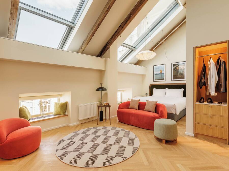 A spacious loft bedroom with skylights, a red sofa, a round rug, and a wooden wardrobe.
