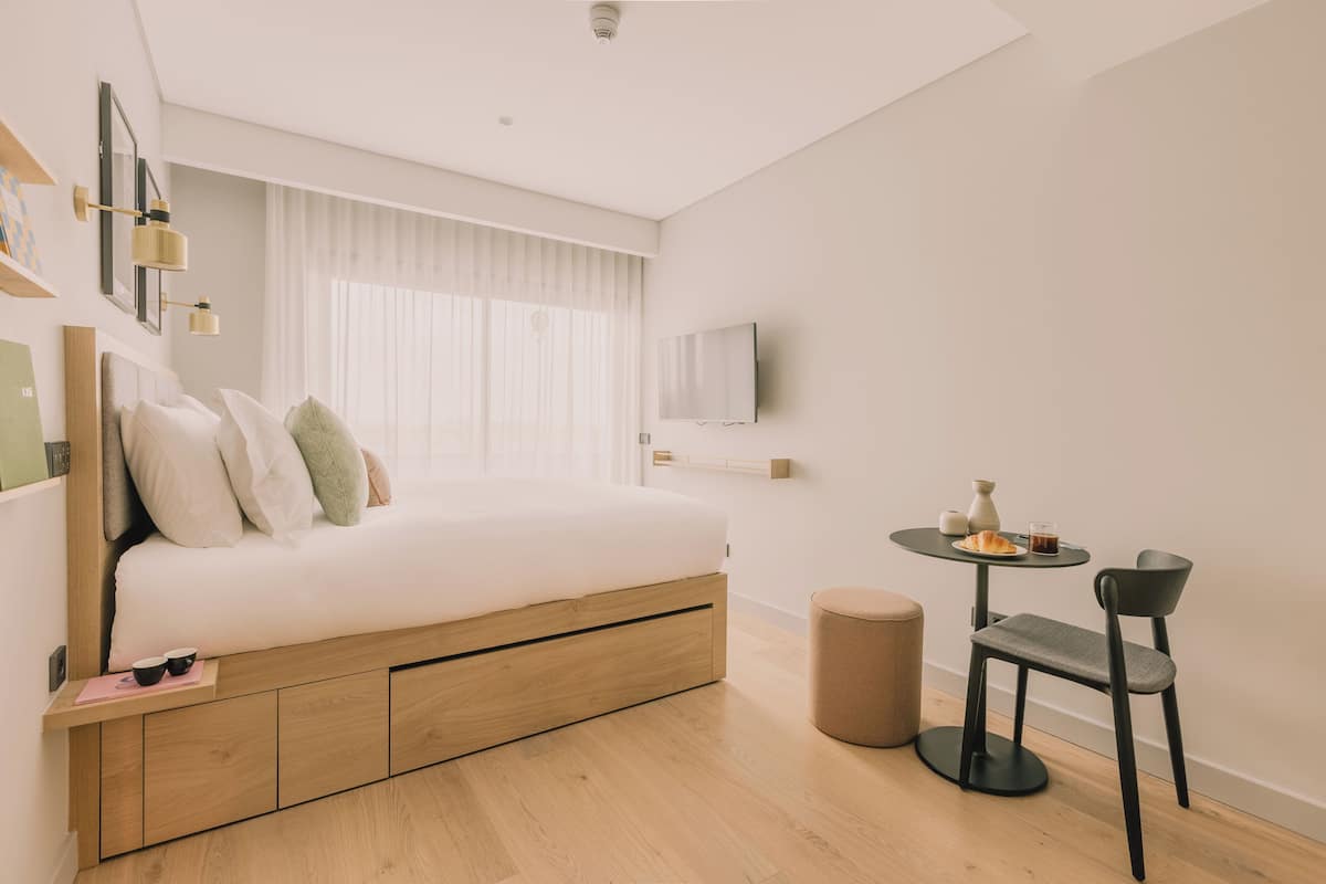 A modern bedroom with a bed, bedside table, and a small round table with a chair.