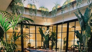 A spacious indoor area with checkered flooring, seating arrangements including sofas and chairs, and large potted plants.