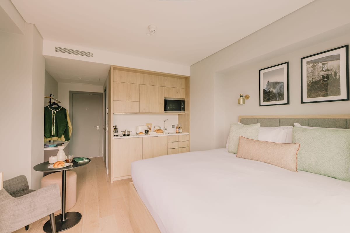 A modern hotel room with a bed, a small kitchenette, a dining area, and a walk-in closet.