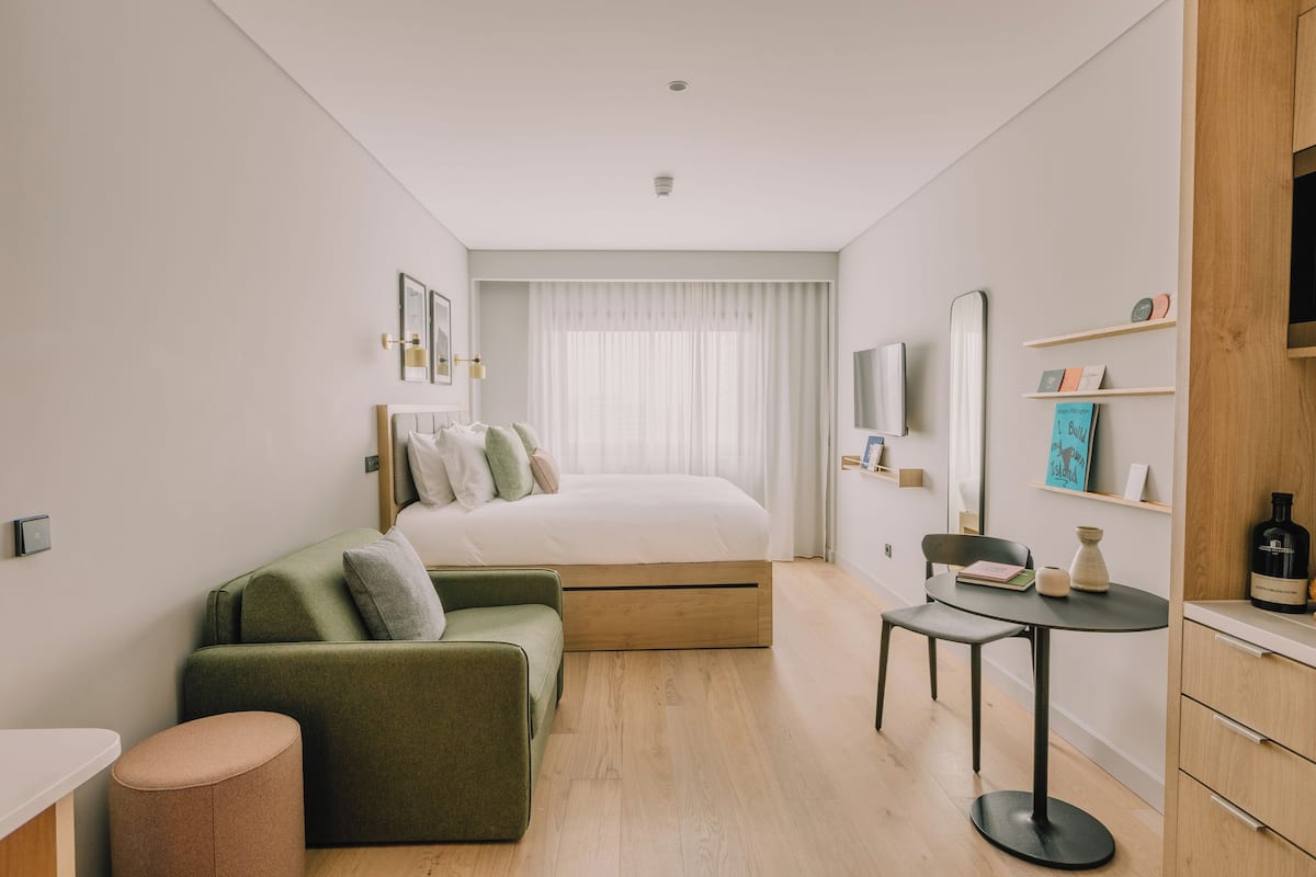 A modern hotel room with a bed, a green sofa, a small table, and a wooden cabinet.