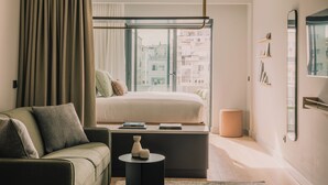 A modern bedroom with a bed, a sofa, a small table, and a large window with a city view.