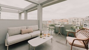 A modern balcony with a sofa, chairs, a small table, and a bottle of wine.