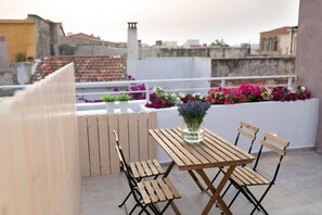 Ein Holztisch mit Stühlen auf einer Dachterrasse, Blick auf Gebäude und ein Blumenbeet.