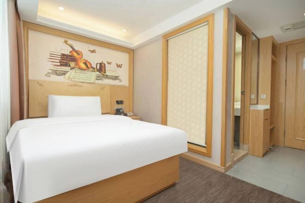 A hotel room with a bed, a nightstand, a wall-mounted artwork, and a sliding door leading to a bathroom.