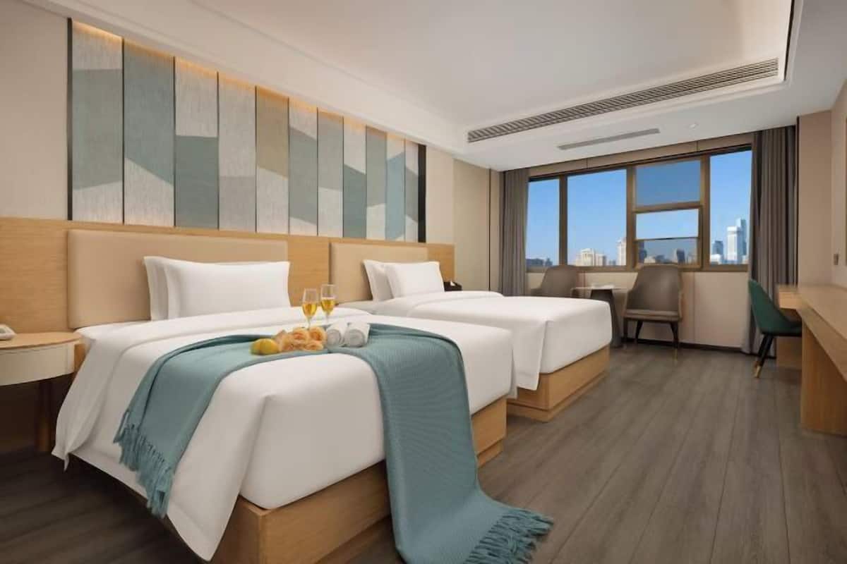 A hotel room with two beds, a desk, and a view of the city.