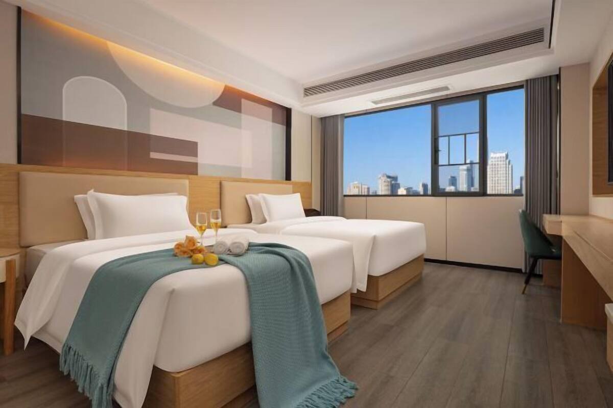 A hotel room with two beds, a desk, a large window with a city view, and a modern design.