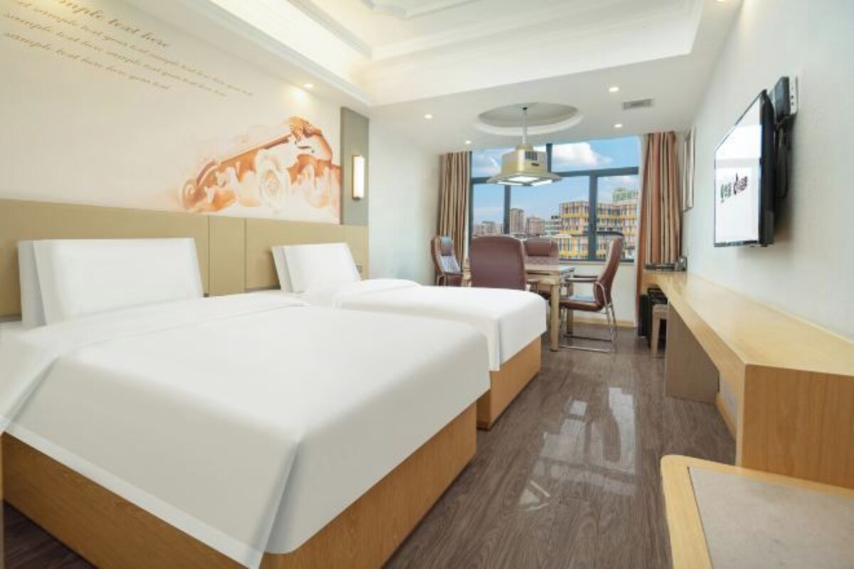 A hotel room with two beds, a desk, a chair, a TV, and a large window with a city view.