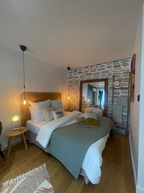 Een slaapkamer met een stenen muur, een houten hoofdbord, een bed met wit beddengoed, een bedlampje en een spiegel.