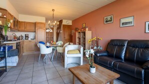 A living room with a black leather sofa, a wooden coffee table, and a dining area with a table and chairs. - Wonderful  villa for 4 people with WIFI and TV (Bruges)