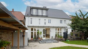 Une maison à deux étages dotée d’un patio couvert et d’un chemin en briques menant à l’entrée.