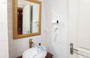 A bathroom with a marble sink, a gold-framed mirror, and a hairdryer mounted on the wall.