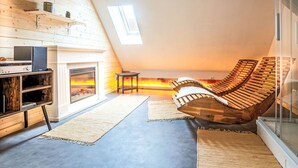 A cozy attic room with a fireplace, wooden lounge chairs, and a skylight. - Lovely apartment for 2 guests with WIFI, TV, terrace and pets allowed (Neustrelitz)