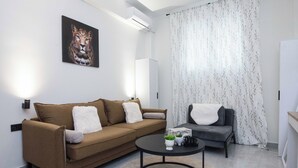 A modern living room with a brown sofa, a grey armchair, a round coffee table, and a painting of a lion on the wall. - Brand New 1 Bd Apt in Trendy Kipseli (Athens)