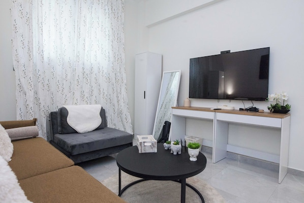 A modern living room with a sofa, a coffee table, a TV, and a desk with a mirror. - Brand New 1 Bd Apt in Trendy Kipseli (Athens)