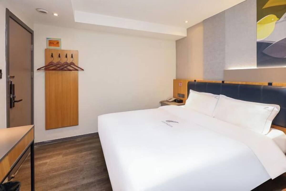 A hotel room with a large bed, a wooden wardrobe, a desk, and a nightstand with a phone.