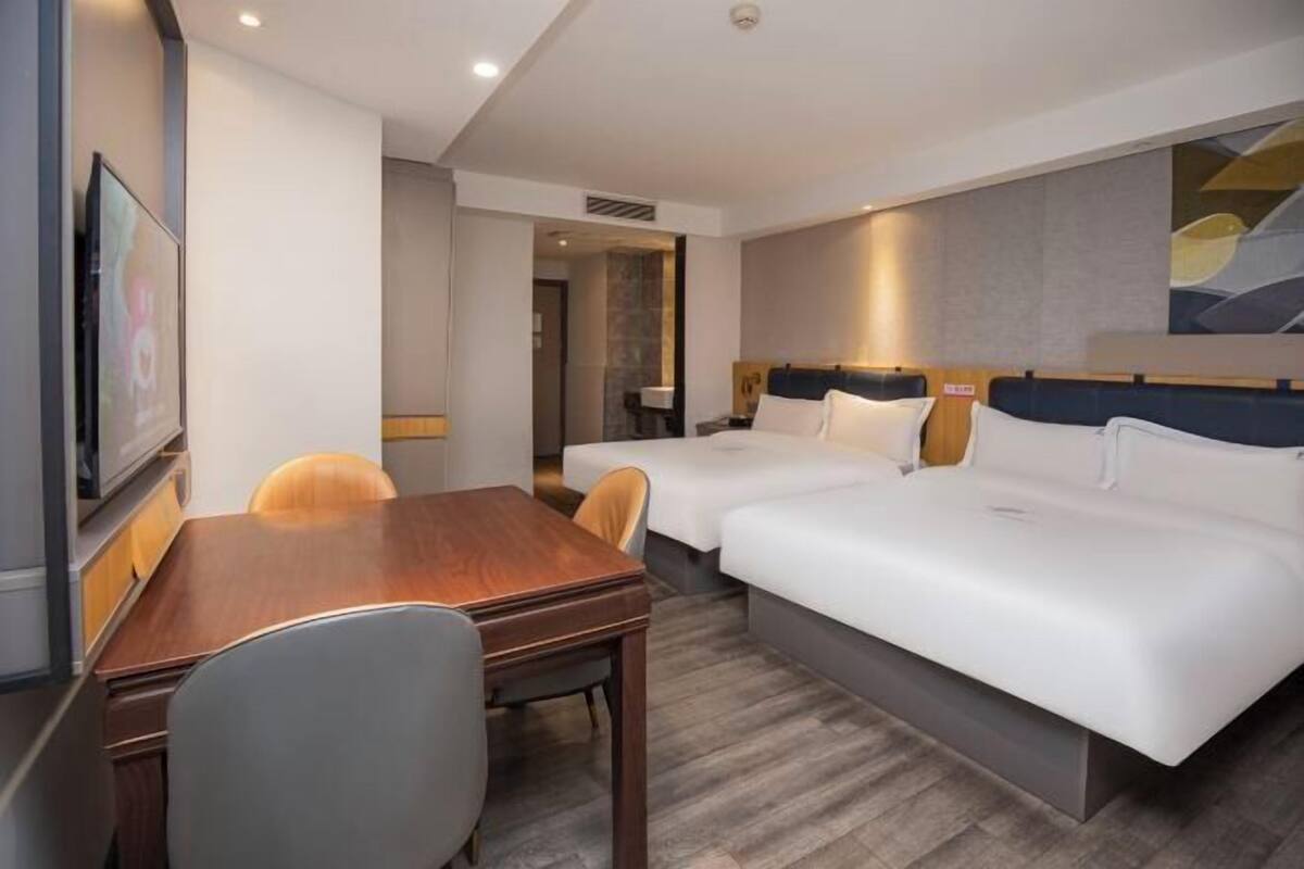 A hotel room with a wooden desk, two single beds, a TV, and a painting on the wall.