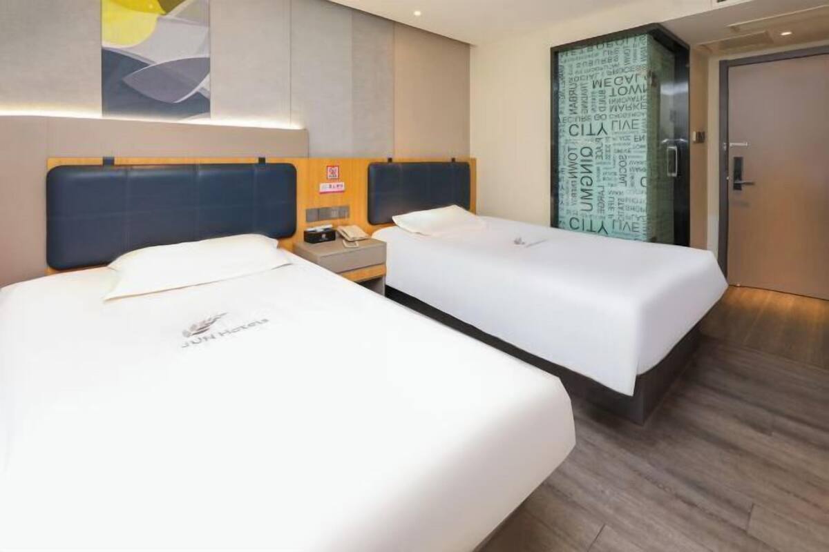 A hotel room with two beds, a nightstand, and a wall with a word cloud design.