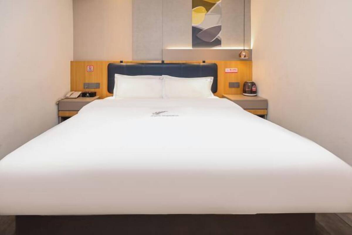 A hotel room with a large bed, wooden headboard, bedside tables with a phone and a coffee maker, and a wall-mounted artwork above the bed.