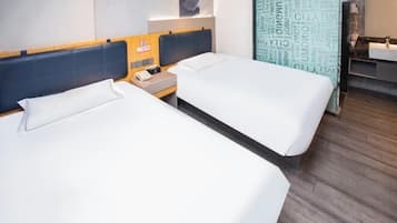 Une chambre d’hôtel avec deux lits, une tête de lit en bois, une table de chevet avec un téléphone et une salle de bain équipée d’un lavabo et d’un miroir.