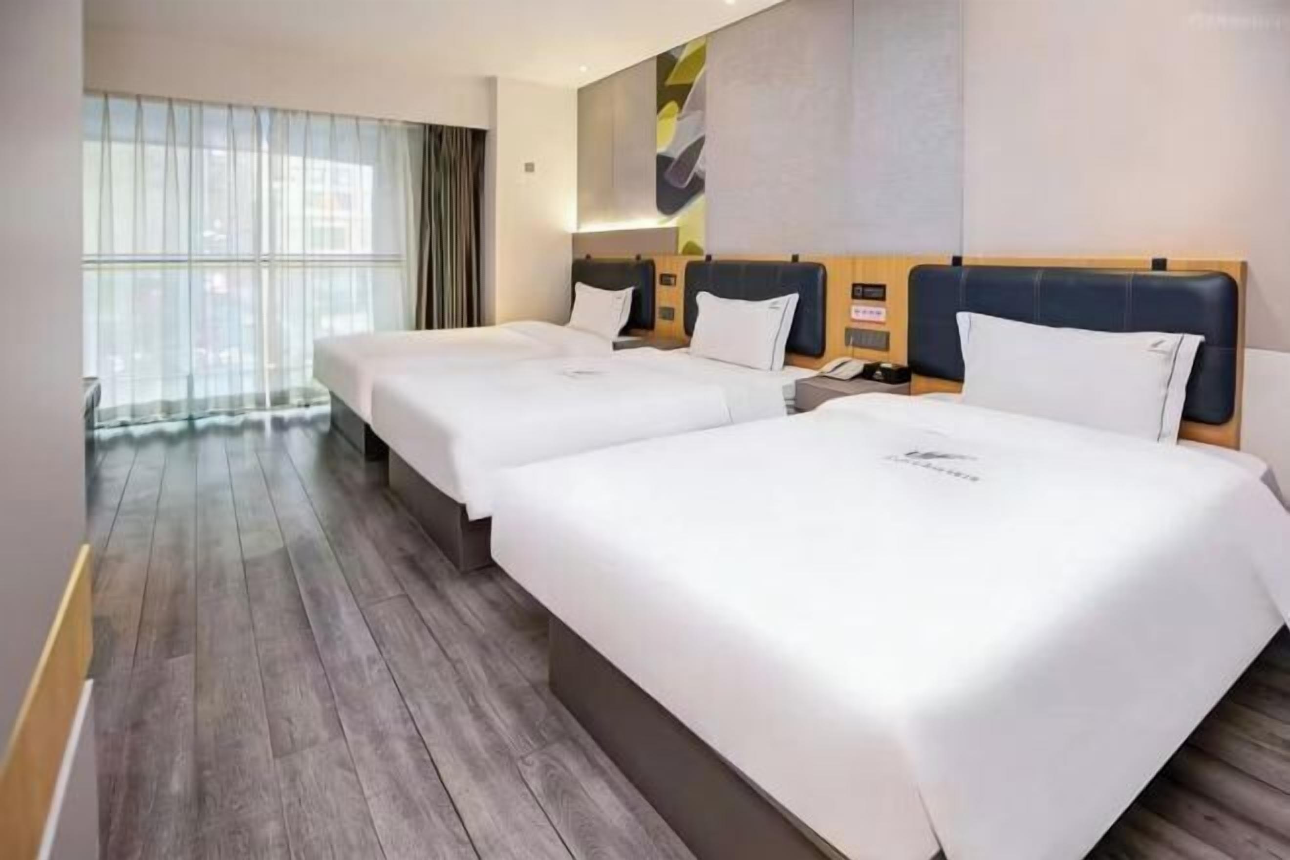 Habitación de hotel con dos camas, suelo de madera, un ventanal grande con cortinas y un diseño moderno en la pared.